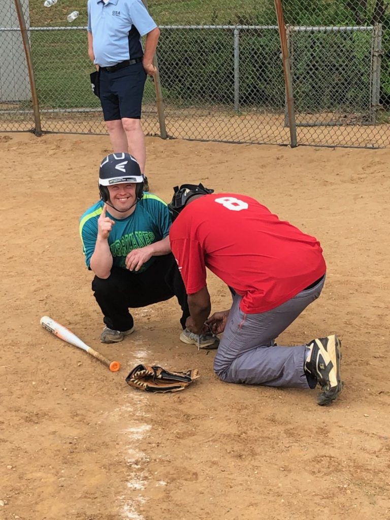 A coach tying an athlete's shoe during a softball game